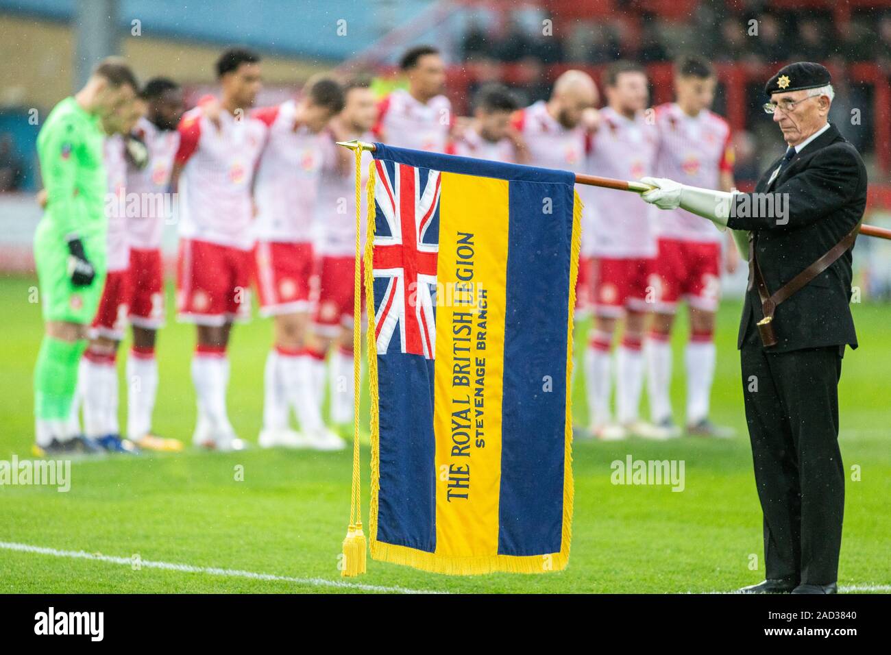 Football players observe minute silence whilst British Legion member lowers banner during Remembrance Sunday commemorations Stock Photo