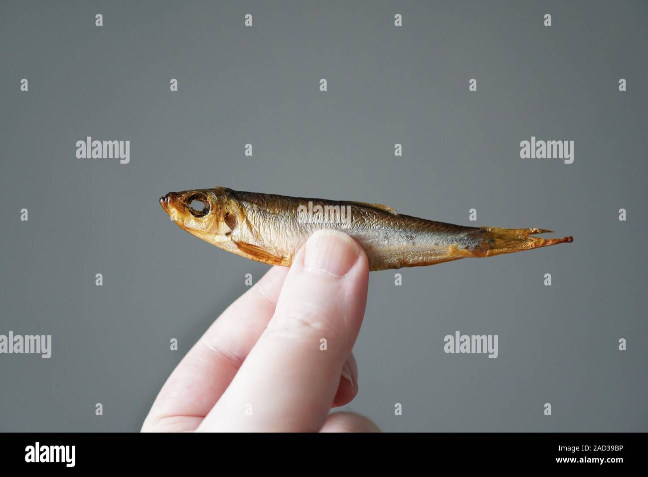 hand of unrecognizable person holding small fish, smoked sprat Stock Photo