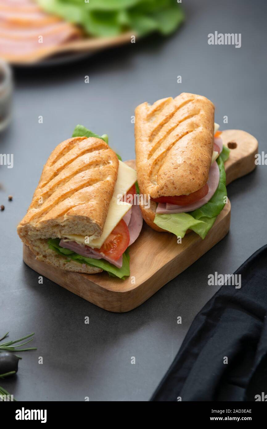 Sandwich with baguette bread, ham, lettuce, tomatoe over dark ...