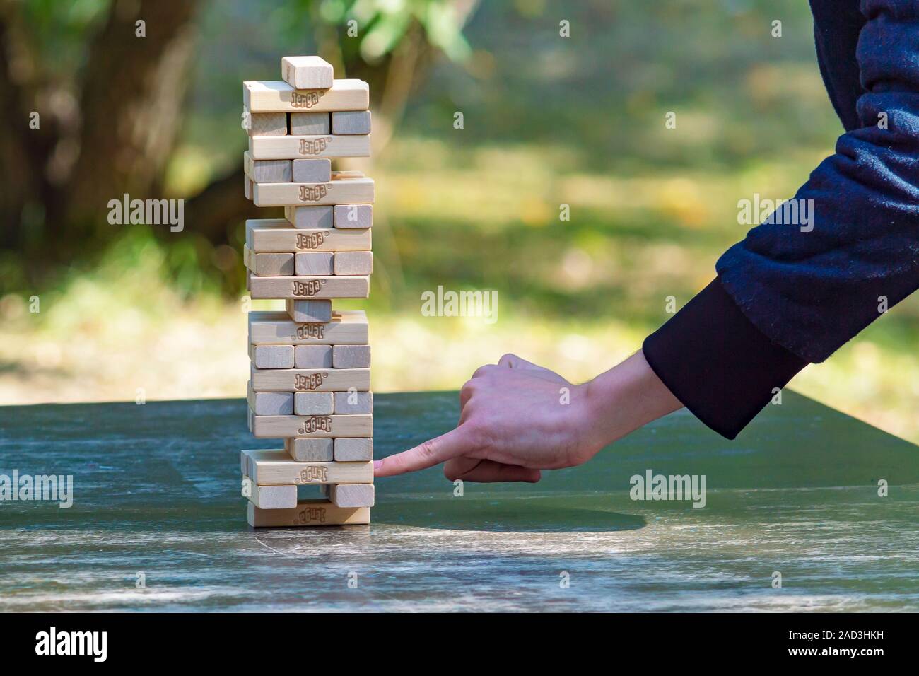 Guy sticks out wooden block from  tower of game jenga. Side view. Concept. Surgut, Russia - September 25, 2019. Stock Photo