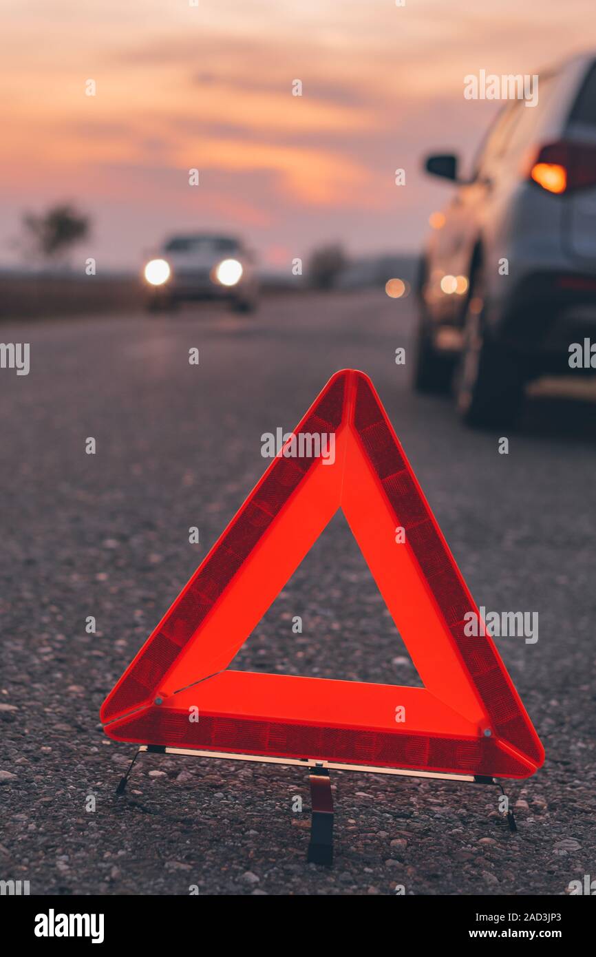 Warning triangle sign on the road in sunset by the broken car, selective focus Stock Photo
