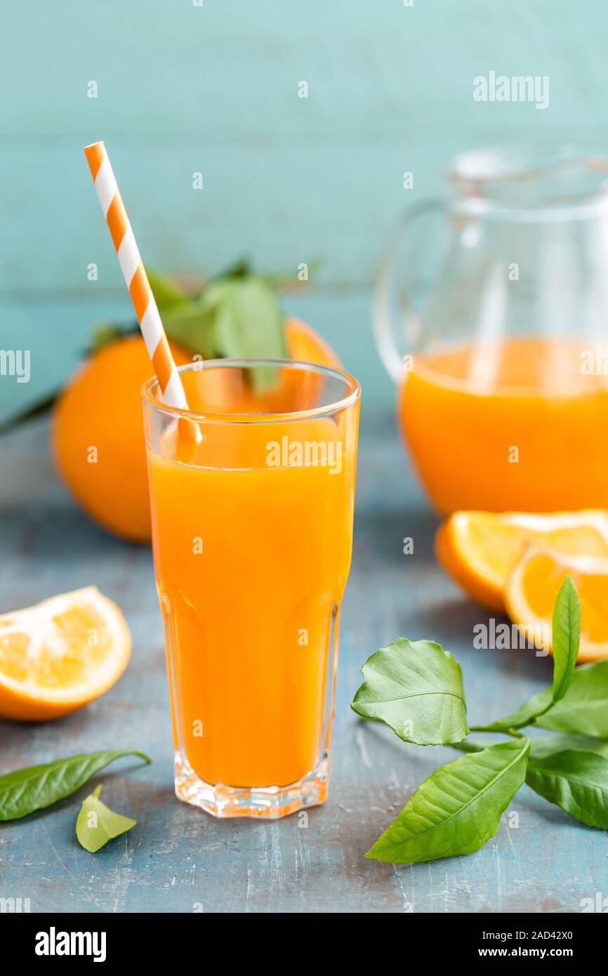 Orange juice in glass and fresh fruits with leaves on wooden background