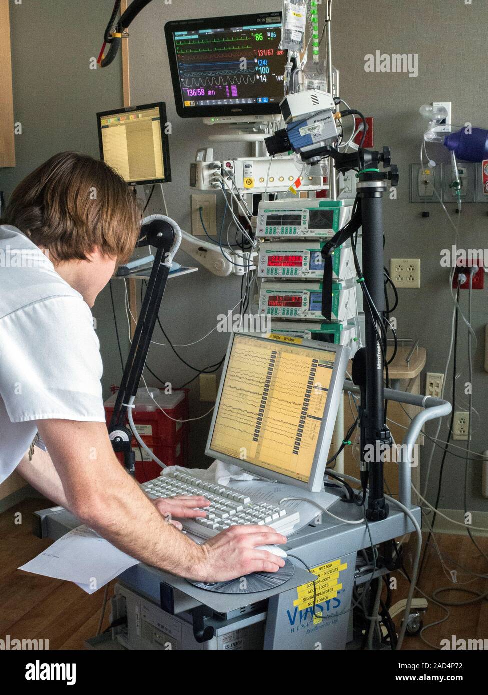 EEG monitoring in intensive care. Technician adjusting bedside EEG (electroencephalogram