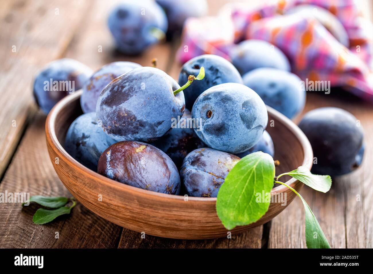 Fresh plums with green leaves on wooden rustic background Stock Photo