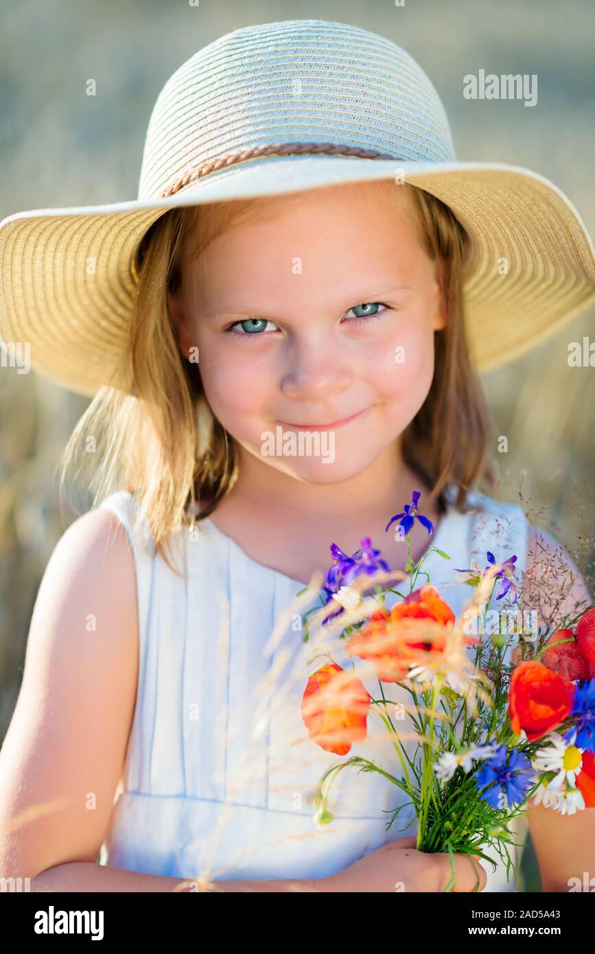 Little cheerful girl in a straw hat with wild flowers red poppy bouquet ...