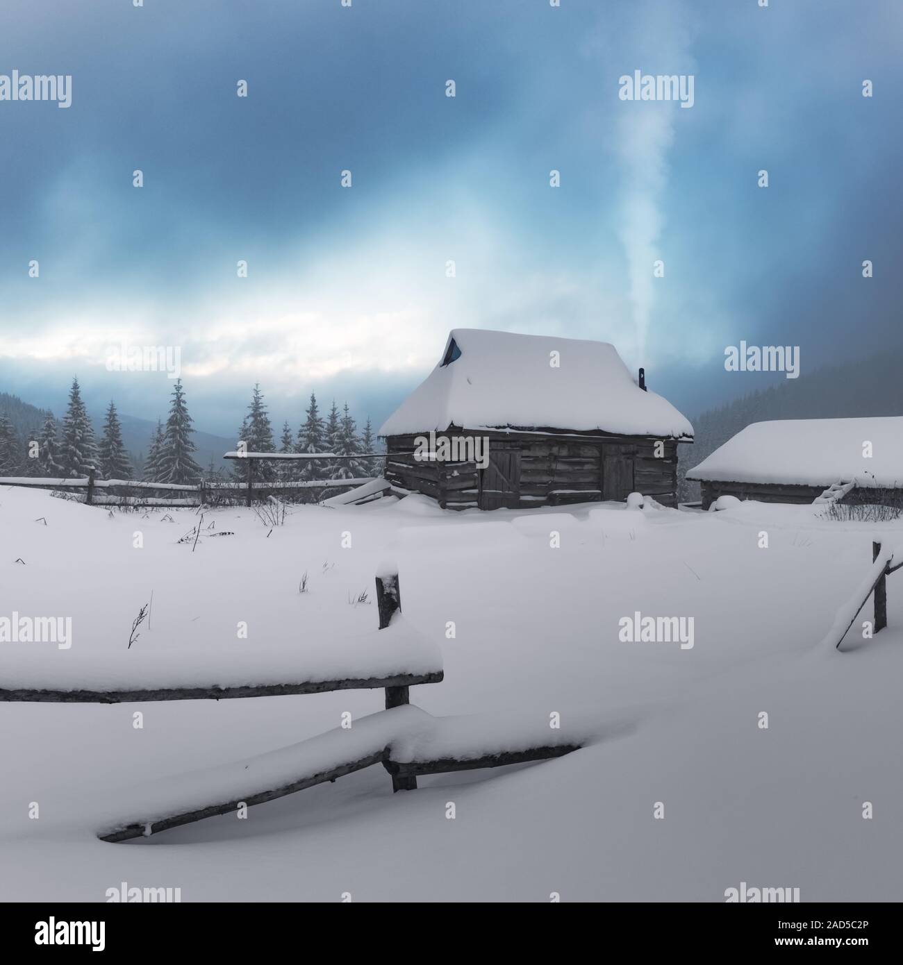 Fantastic winter landscape with wooden house in snowy mountains. Smoke comes from the chimney of snow covered hut. Christmas holiday concept Stock Photo