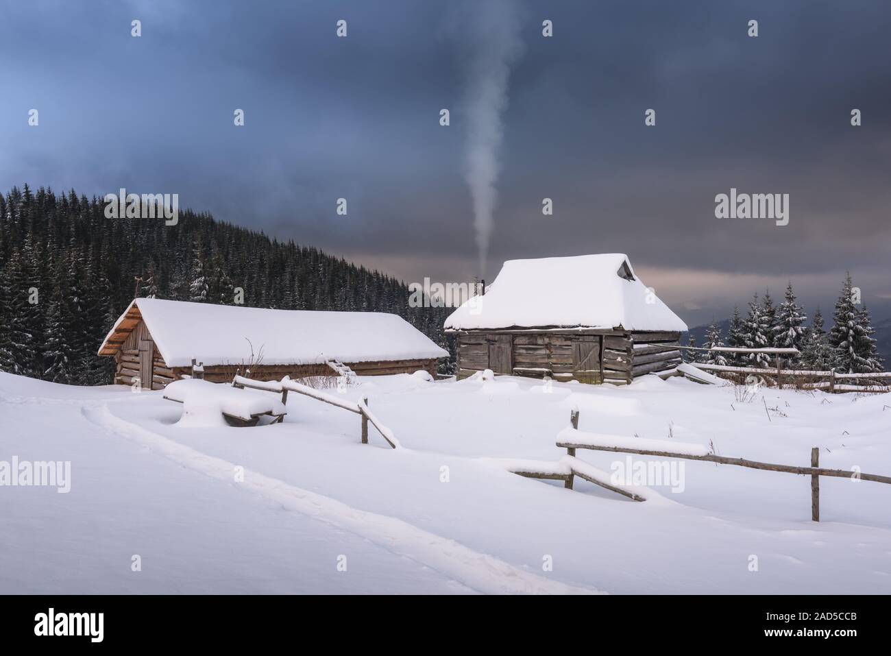 Fantastic winter landscape with wooden house in snowy mountains. Smoke comes from the chimney of snow covered hut. Christmas holiday concept Stock Photo