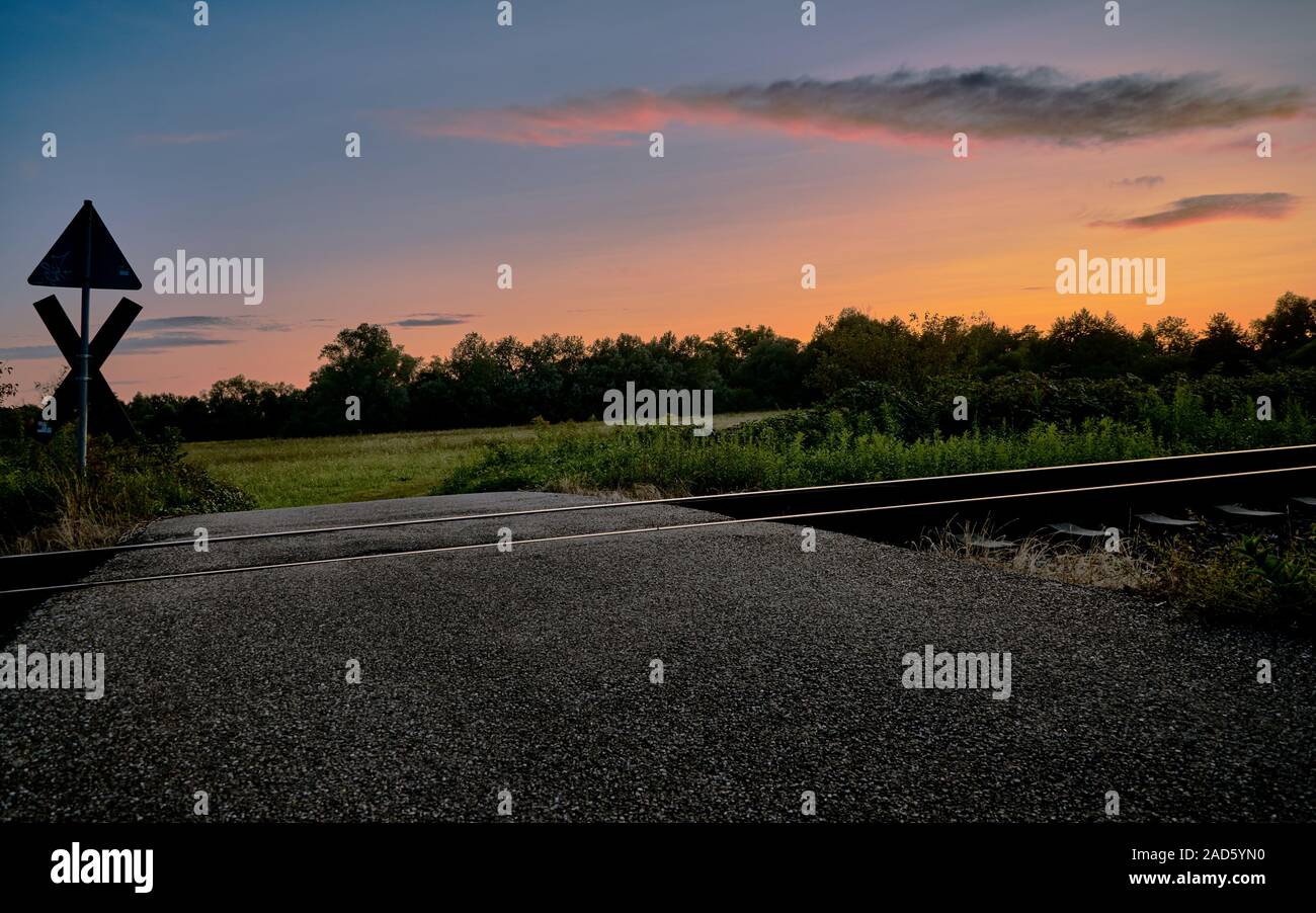 Railroad tracks and a railway crossing infront of beautiful nature and the sunset Stock Photo