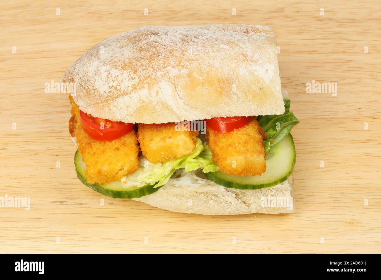 Fish fingers and salad in a ciabatta roll on a wooden chopping board Stock Photo