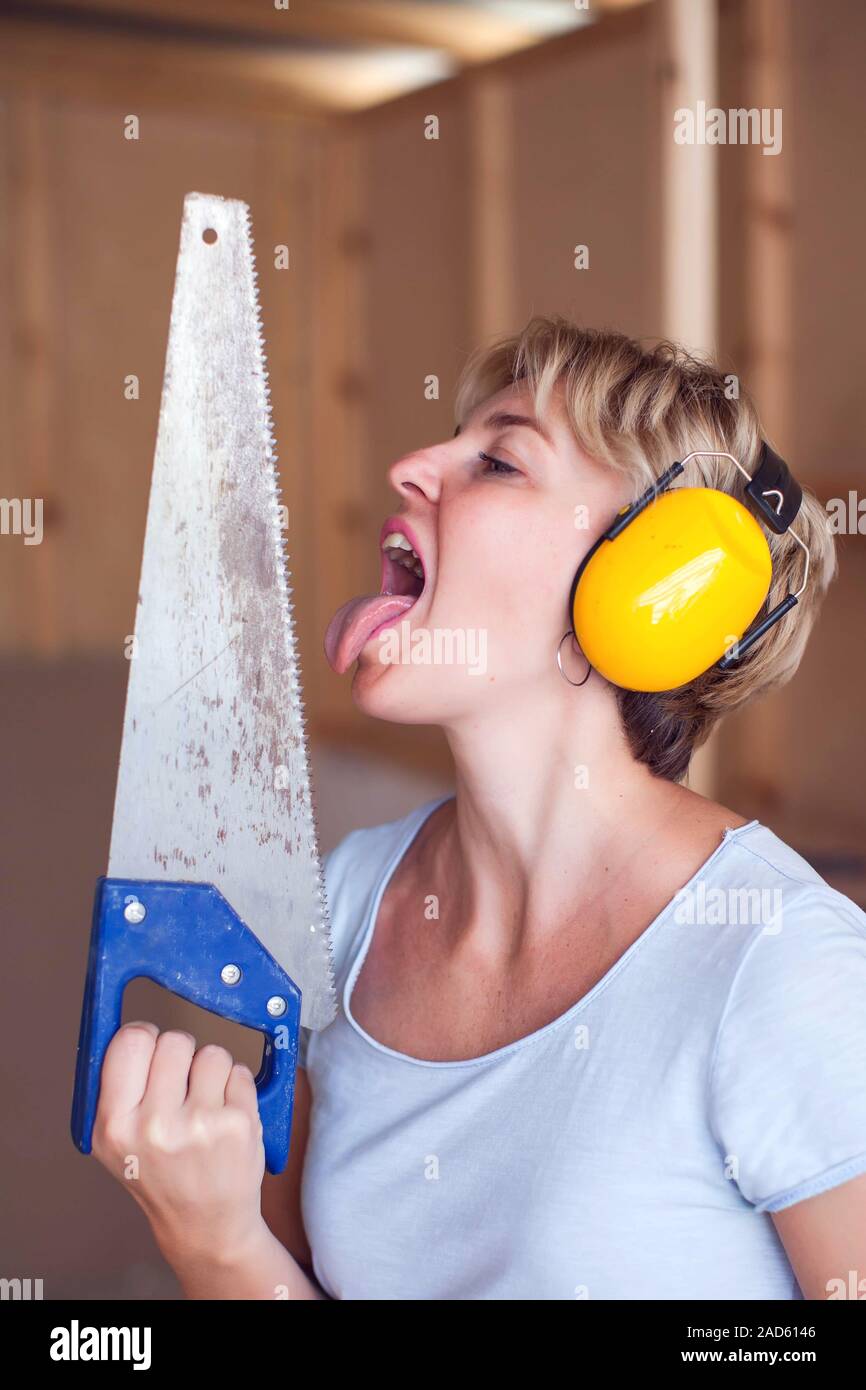 Handy woman with short hair with headphones works with saw, try to licks it. Stock Photo