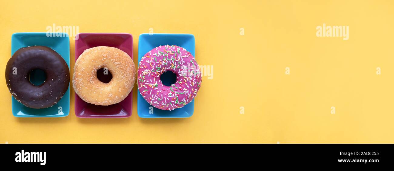 Three different donuts, on a plate on yellow background Stock Photo