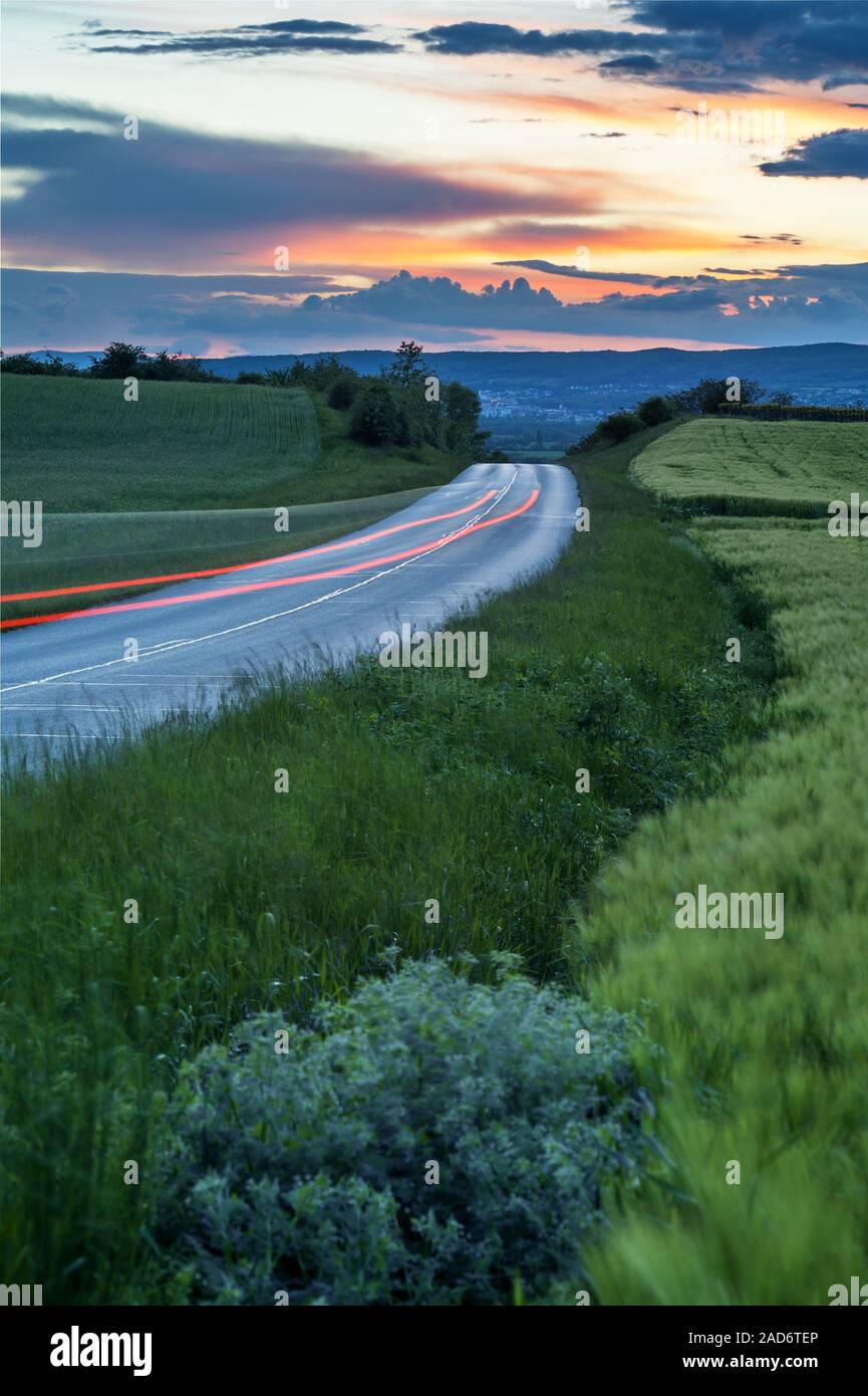 Rural road between fields in the sunset with a PKw red brake light Stock Photo