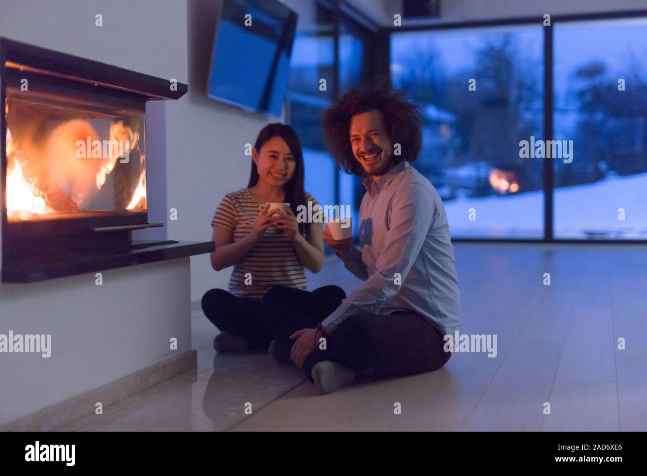 happy multiethnic couple sitting in front of fireplace Stock Photo Alamy