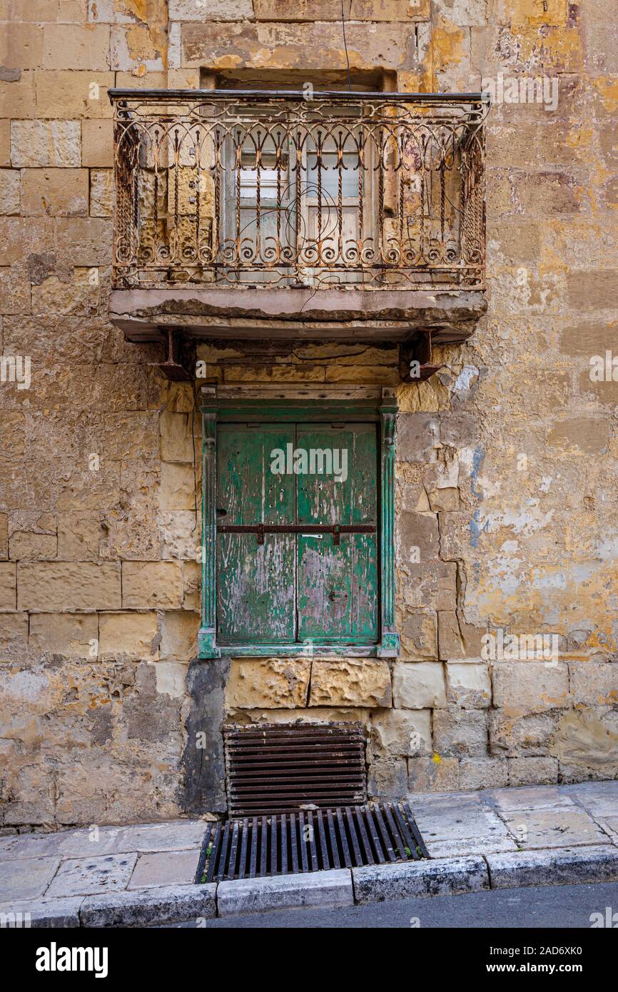 A very old tradional Maltese balcony with rusting but ornate balcony rail above a green painted shuttered and barred window in Valletta, Malta. Stock Photo