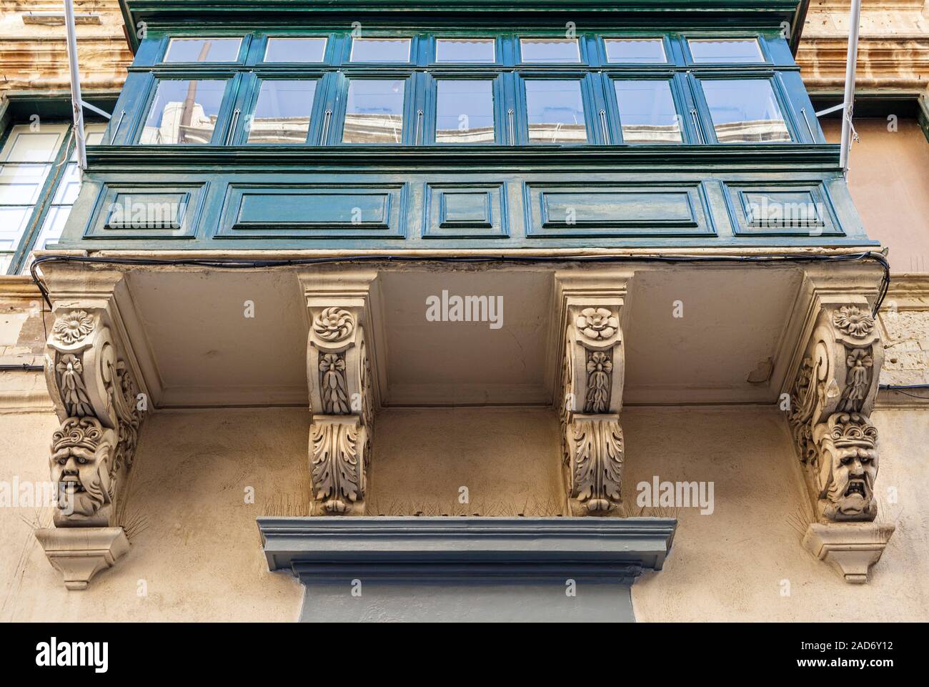 Traditional Maltese enclosed balcony with carved supports known as saljaturi. The faces were intended to ward off evil spirits. Valletta, Malta. Stock Photo