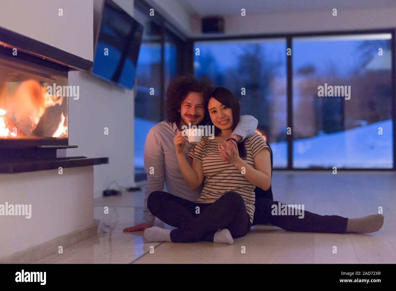 happy multiethnic couple sitting in front of fireplace Stock Photo Alamy