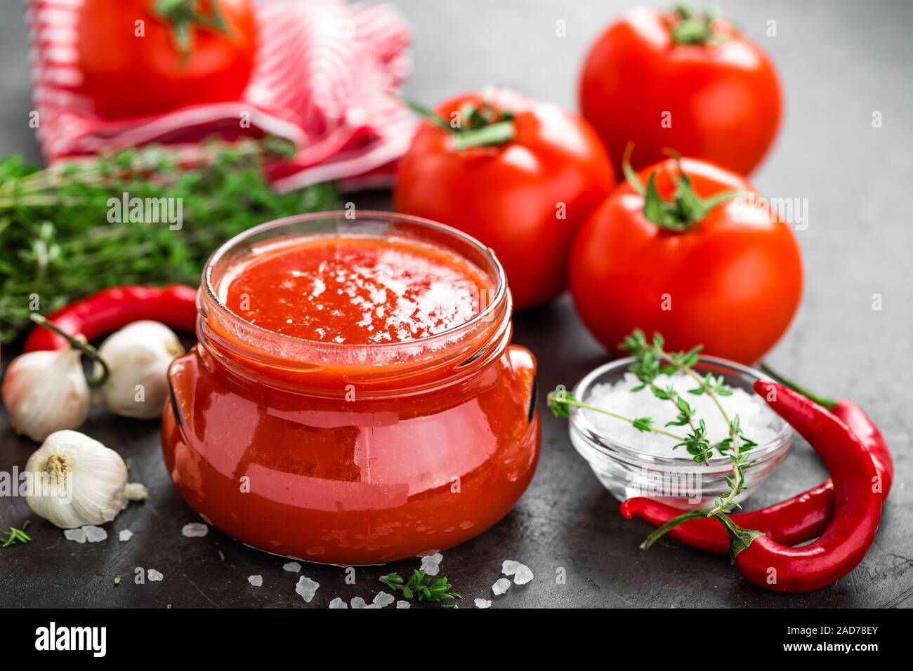 Tomato paste, puree in glass jar and fresh tomatos on dark background
