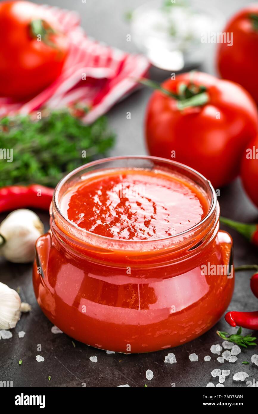 Tomato paste, puree in glass jar and fresh tomatos on dark background