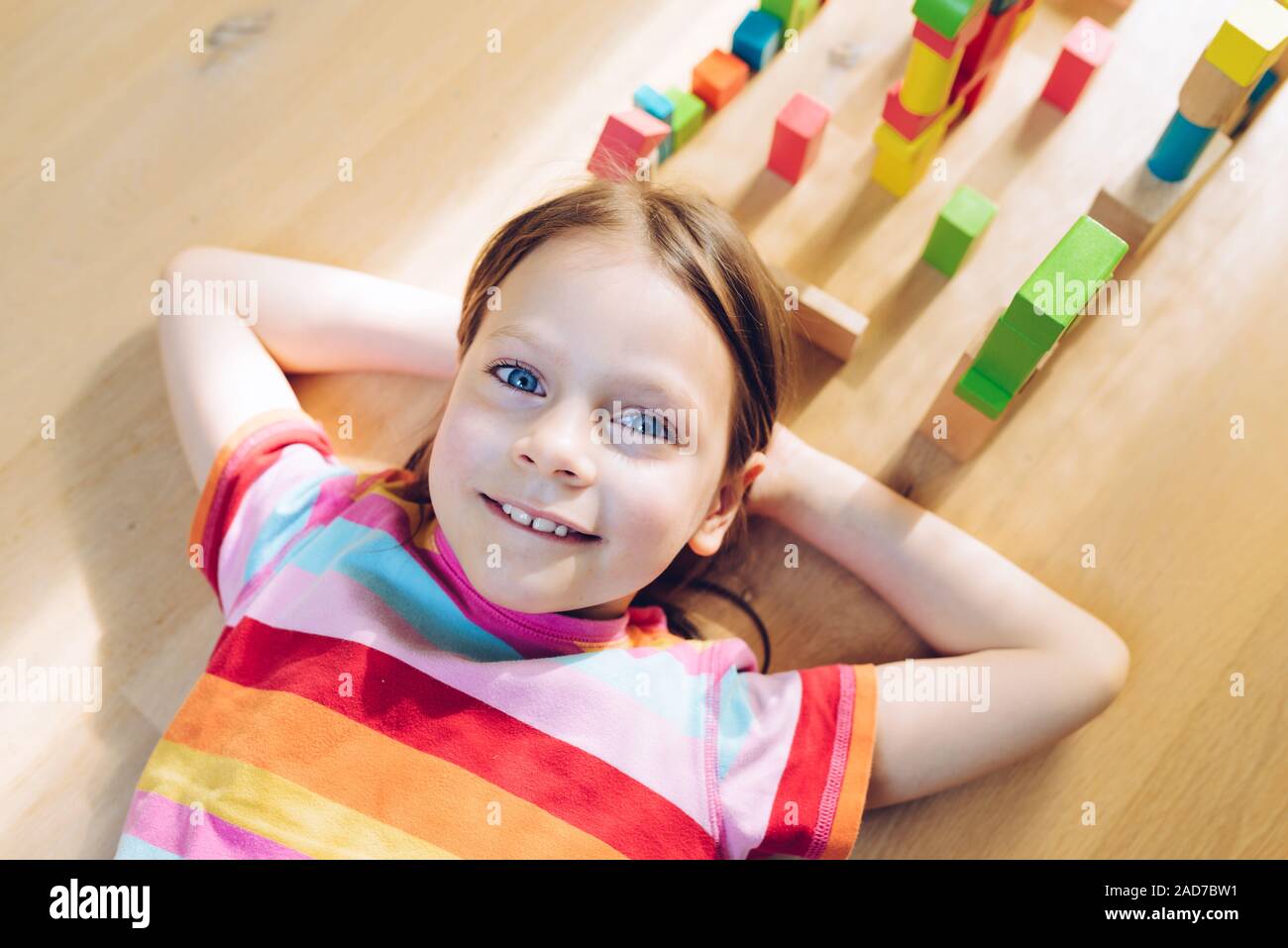 Amused little girl lying on her back on the floor colorful wooden