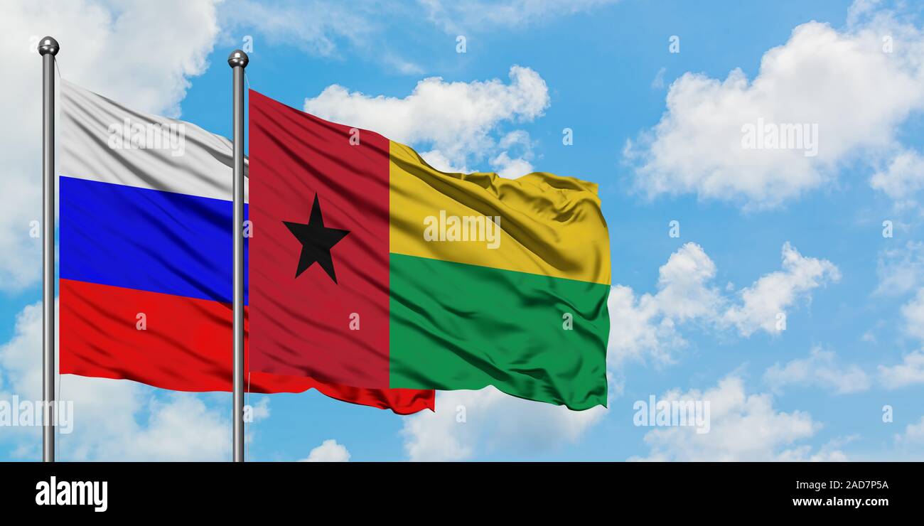 Russia and Guinea Bissau flag waving in the wind against white cloudy blue sky together. Diplomacy concept, international relations. Stock Photo