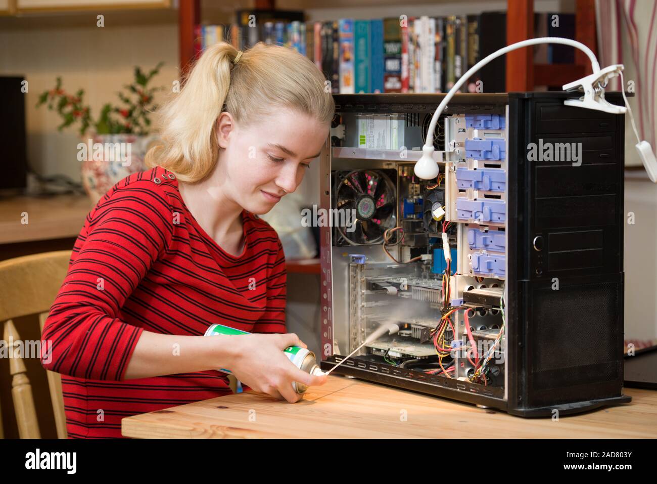 Teenage girl using a can of compressed air to clean the inside of a PC