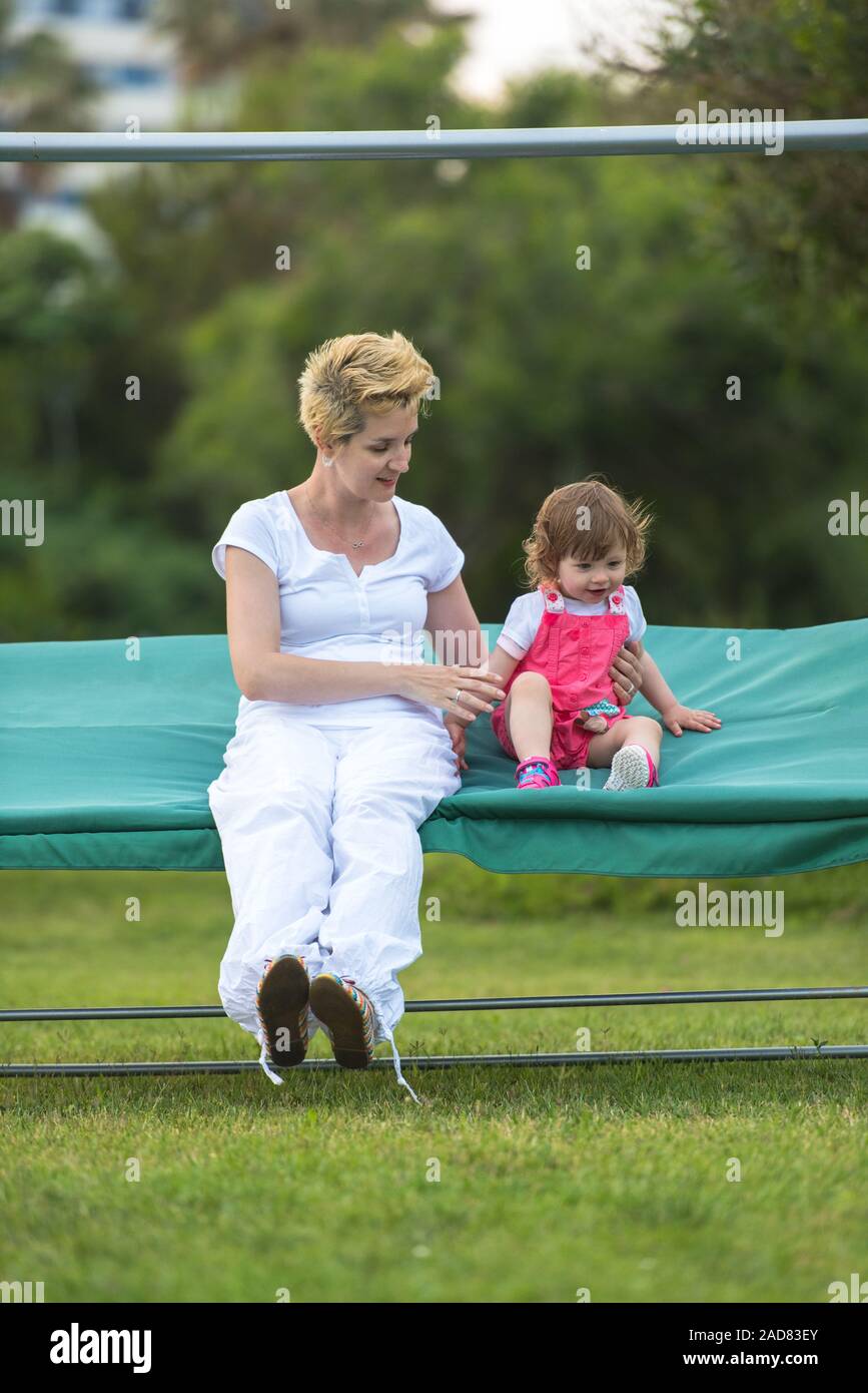 Mother And Little Daughter Swinging At Backyard Stock Photo