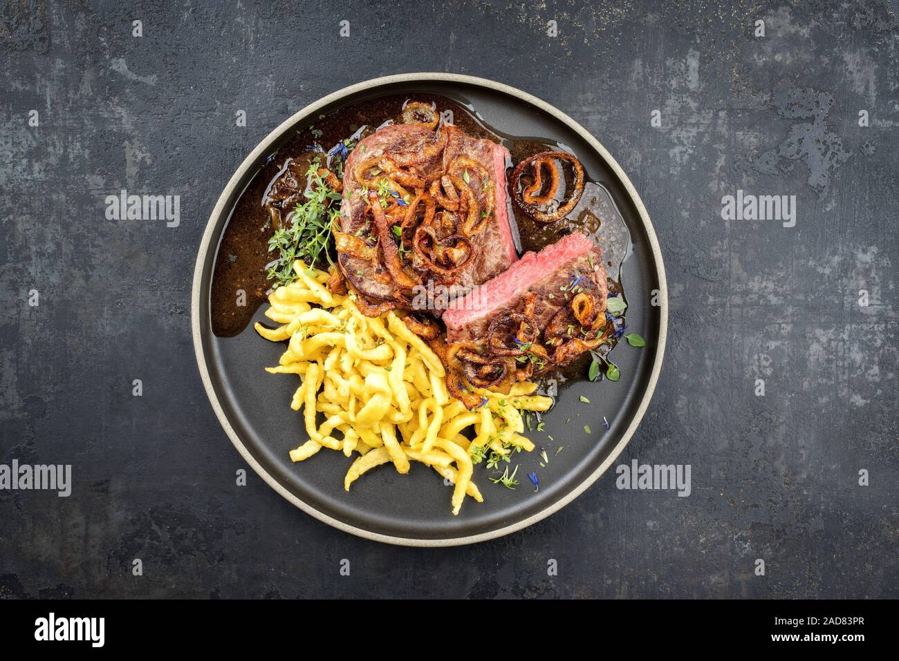 Traditional dry aged sliced roast beef with fried onion rings and Swabian spaetzle as top view on a modern style plate with brow Stock Photo