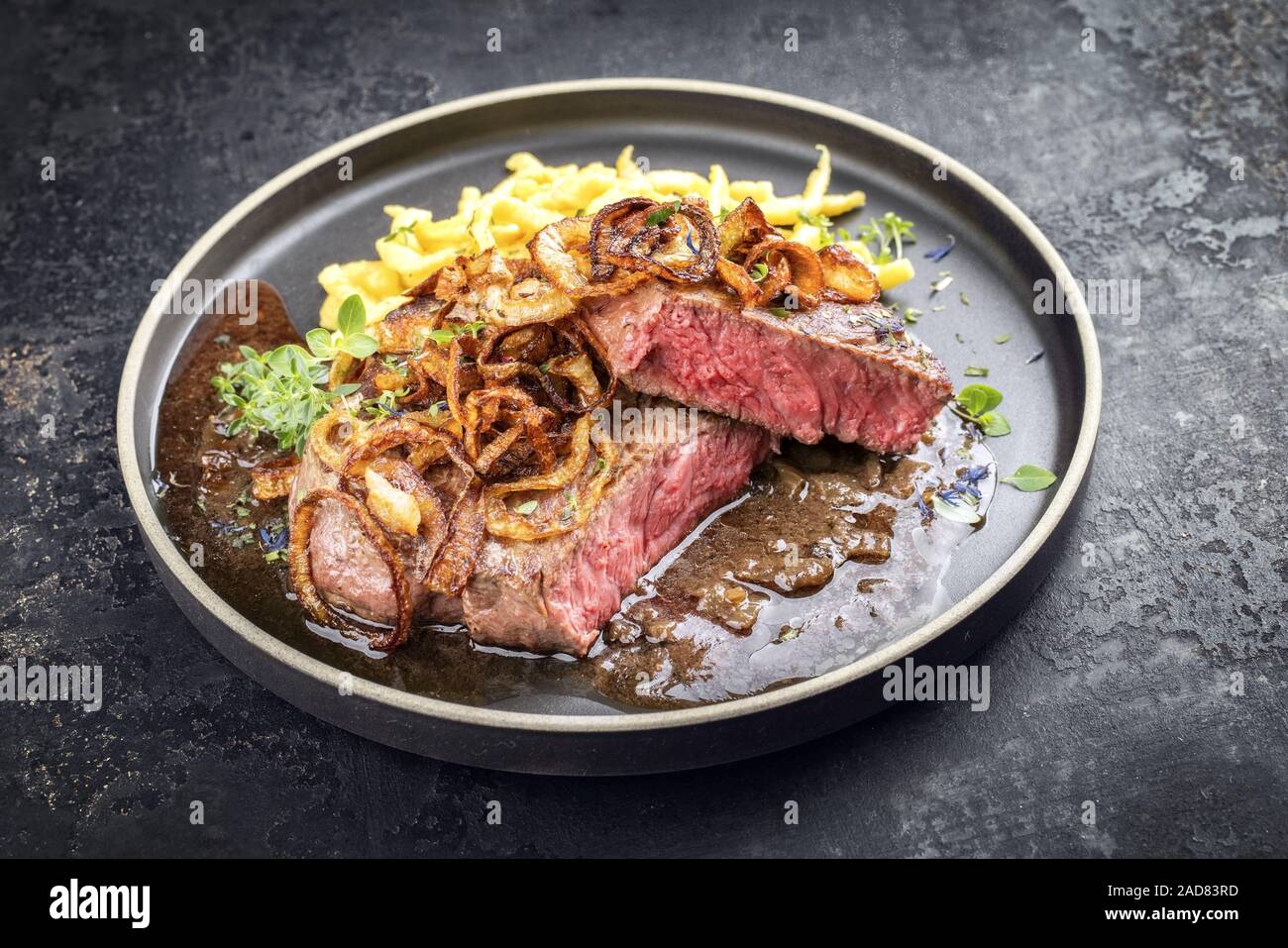 Traditional dry aged sliced roast beef with fried onion rings and Swabian spaetzle as closeup on a modern style plate with brown Stock Photo