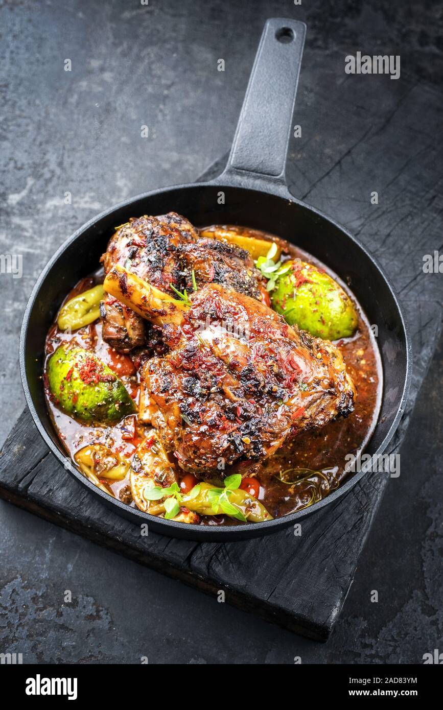 Traditional barbecue leg of lamb with lemon and tomatoes as closeup in a castiron skillet Stock