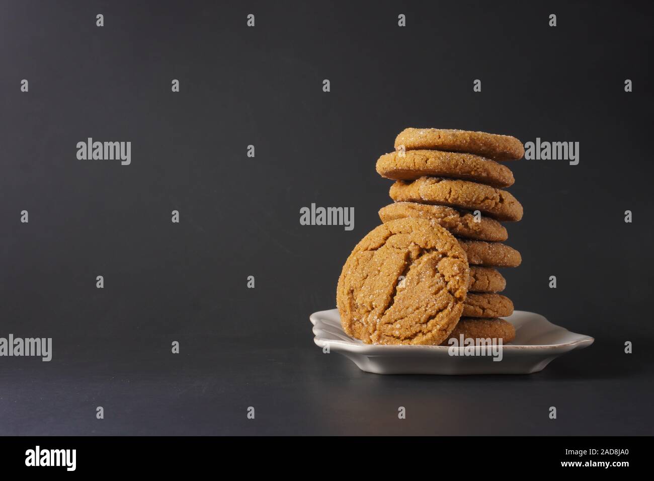 A ginger cookie leans on a stack of cookies on a white plate with a black background; copy space Stock Photo
