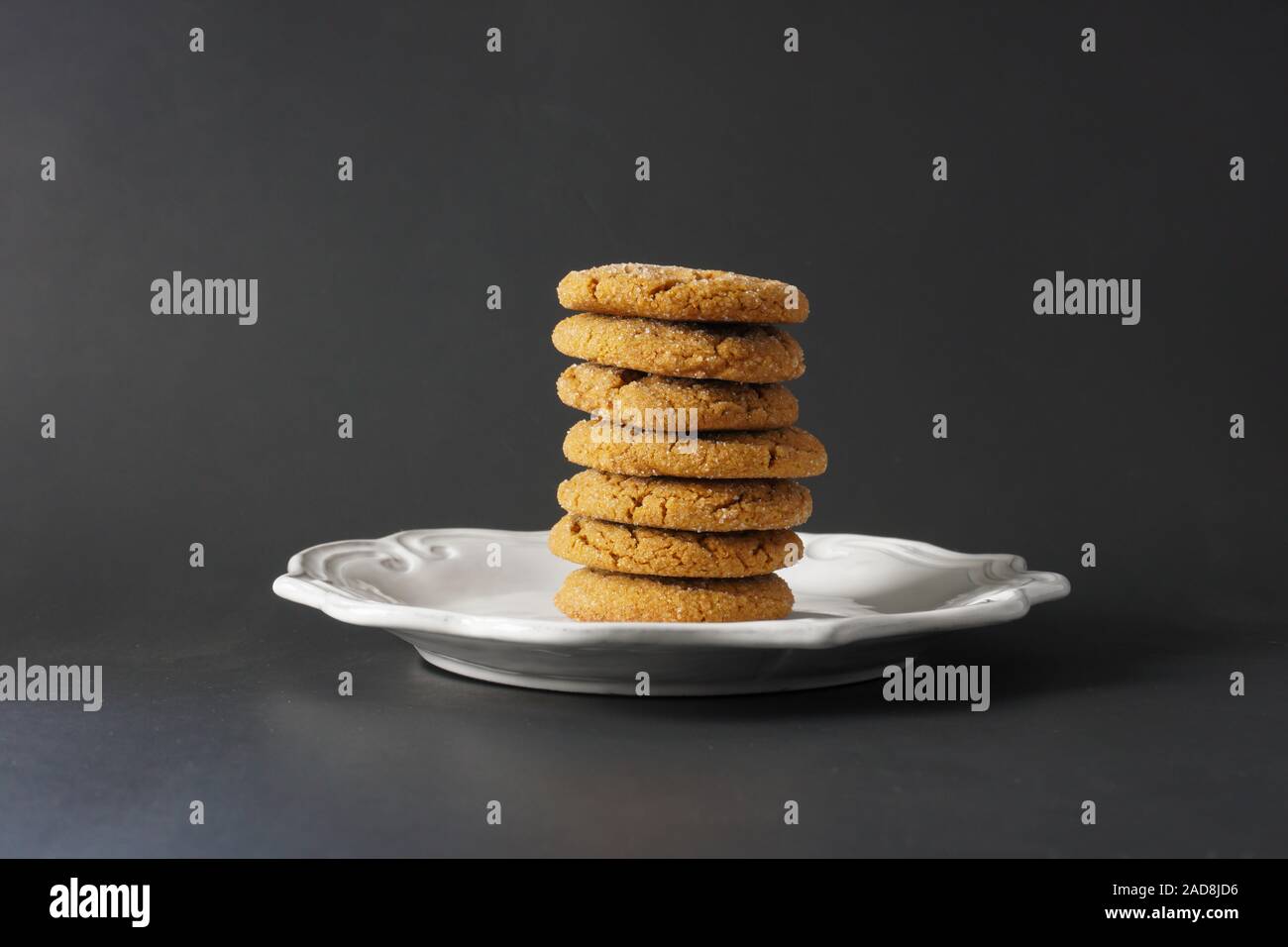 A pile of chewy gingerbread cookies stacked high on a white plate with a black background; copy space Stock Photo