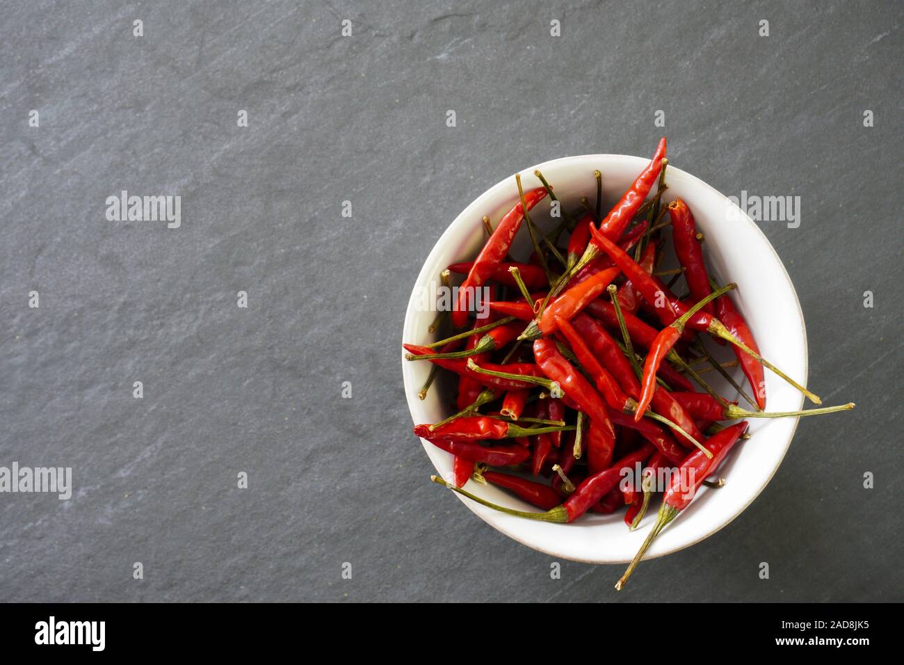 A bowl full of red chiles on a gray background with copy space on the ieft of the image Stock Photo