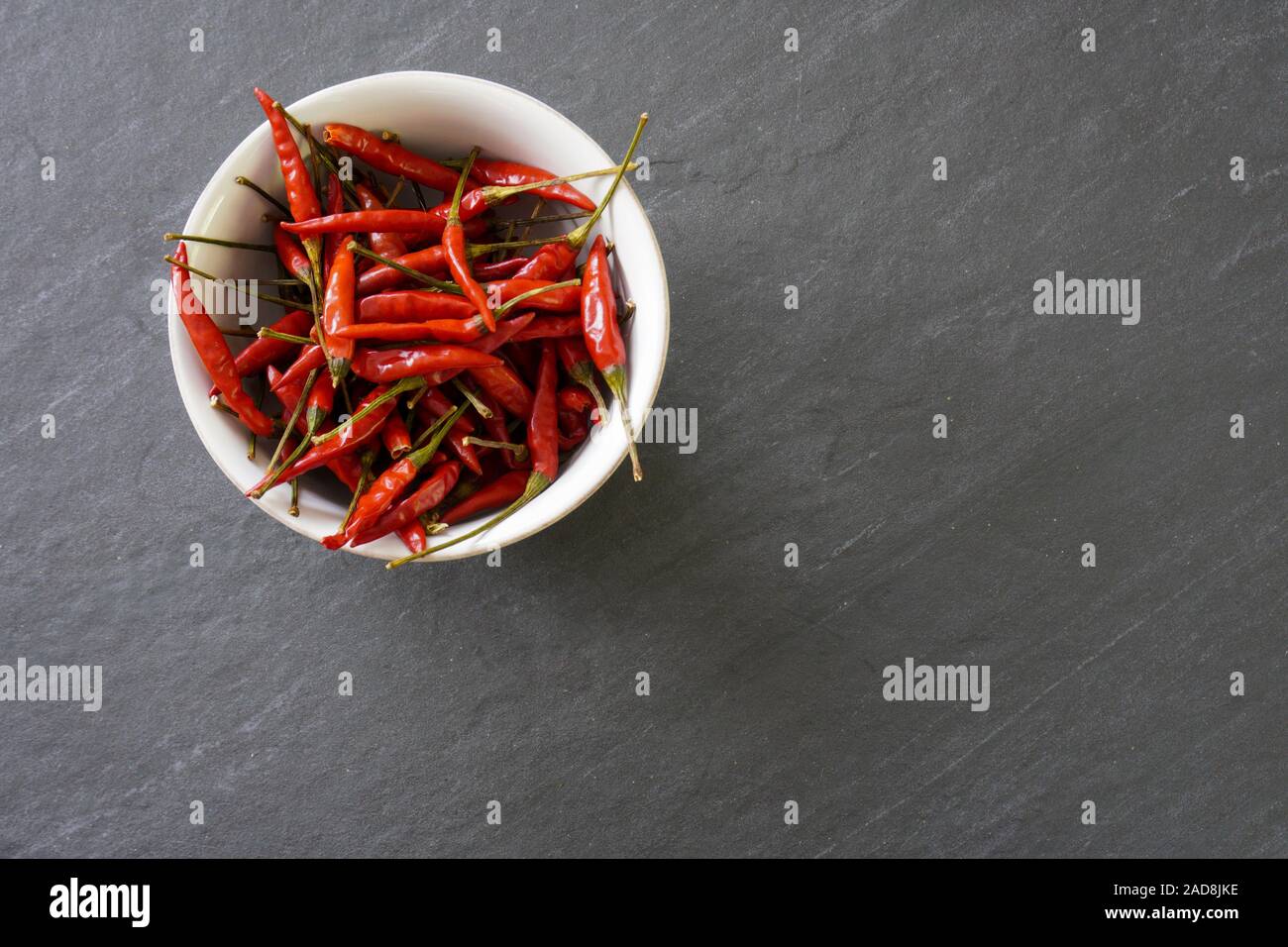 A bowl of bright red chiles on a gray background viewed from above with copy space on the right side and bottom of image Stock Photo