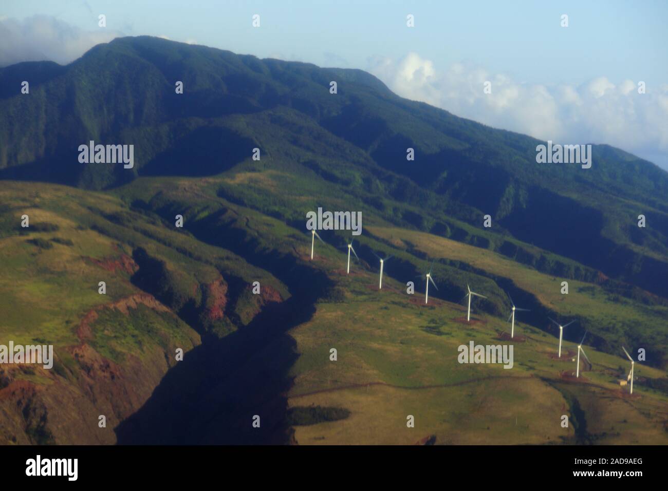 Aerial view of Modern Windmills spin on hillside with windy road up to mountain top on the island of Maui. Stock Photo