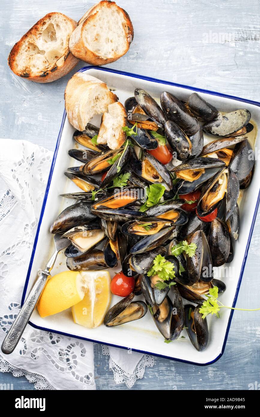 Traditional barbecue Italian blue mussel with baguette and tomatoes in white wine as top view on a tray Stock Photo