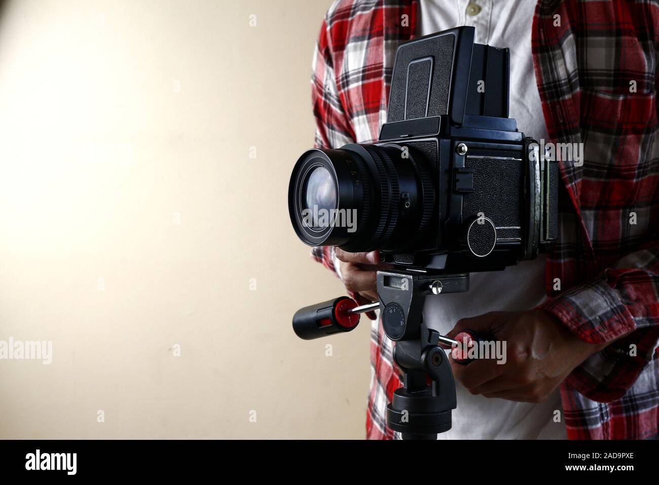 Photo of an adult man holding an old and vintage medium format film camera on a tripod. Stock Photo