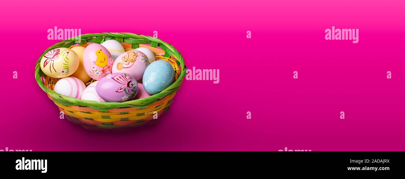 Wicker basket with Easter eggs hand painted on color tabletop background Stock Photo