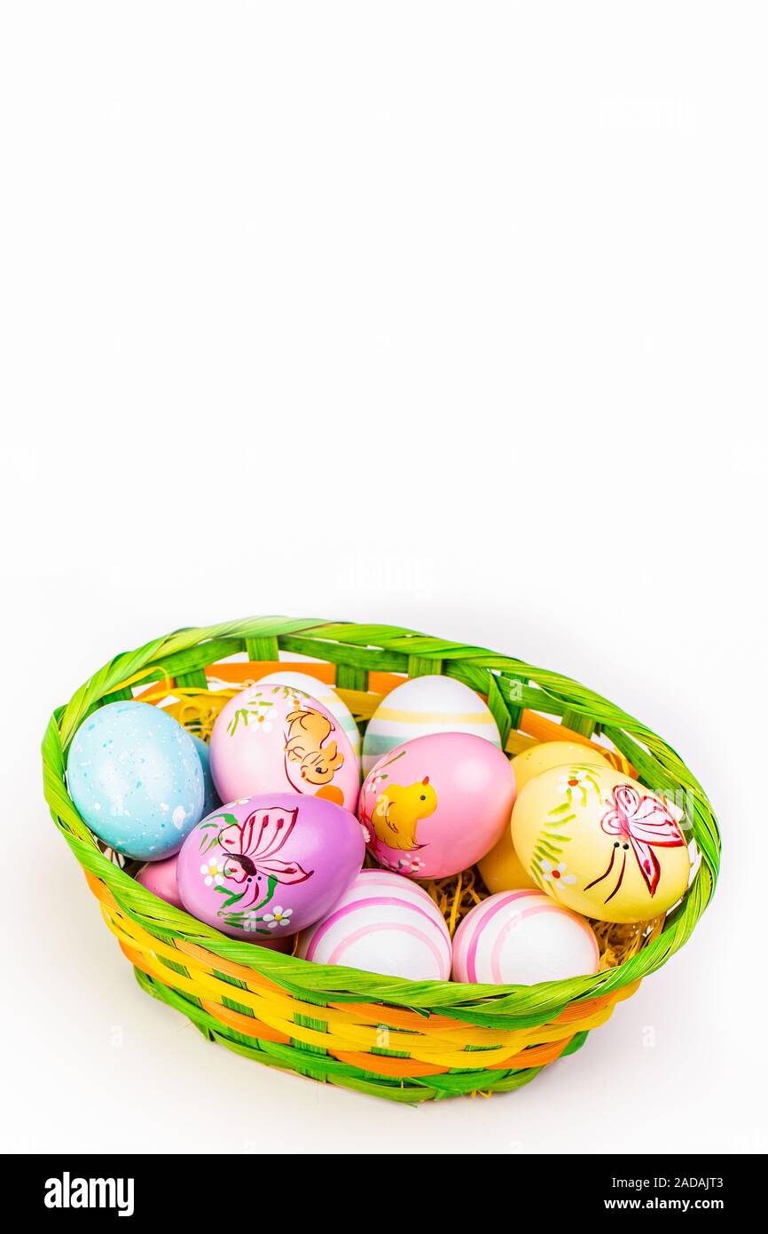 Wicker basket with Easter eggs hand painted on white tabletop background Stock Photo