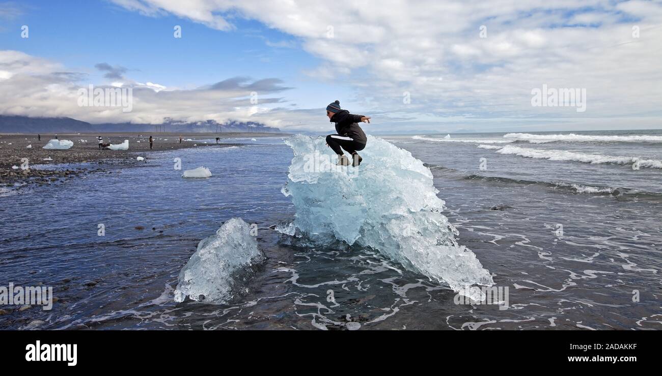Young man on small glacier iceberg at the beach 