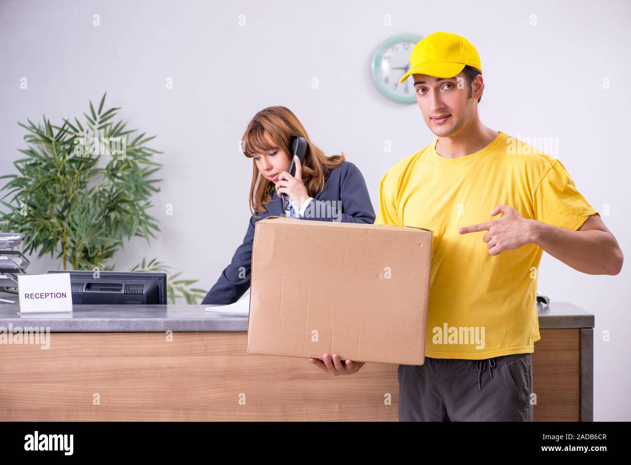 Young male courier delivering box to hotel's reception Stock Photo
