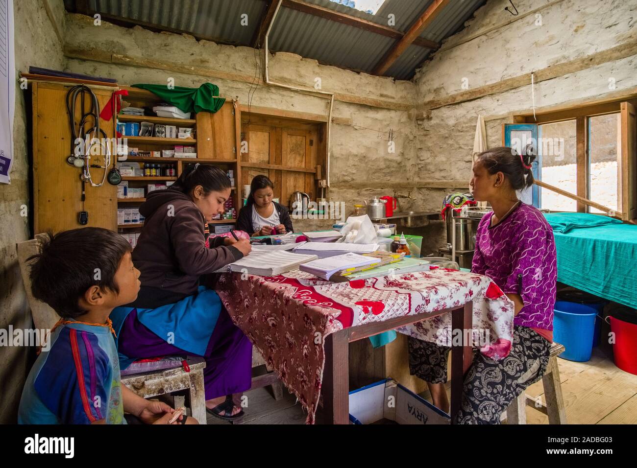 A femal doctor is practising in the medical station of the village, two patients waiting for treatment Stock Photo