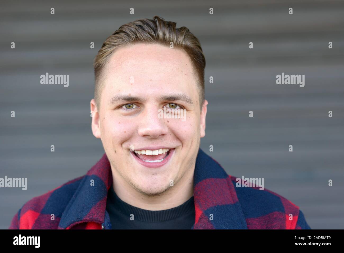 Happy attractive young man with a warm friendly smile posing in front ...