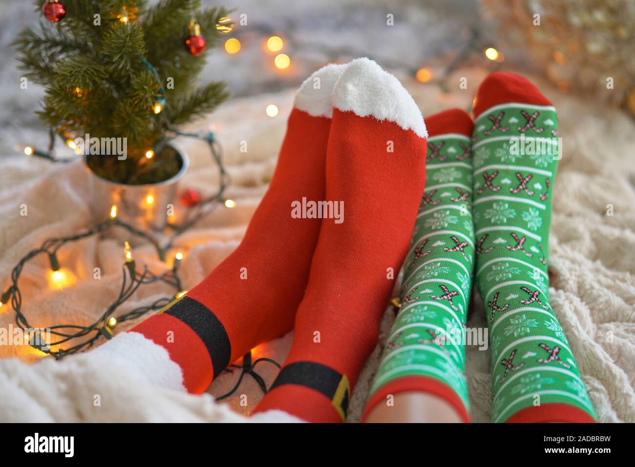 Feet in christmas socks near the Christmas tree. Couple sitting at the blanket, relaxes warming up their feet in woollen socks. Winter and Christmas h Stock Photo