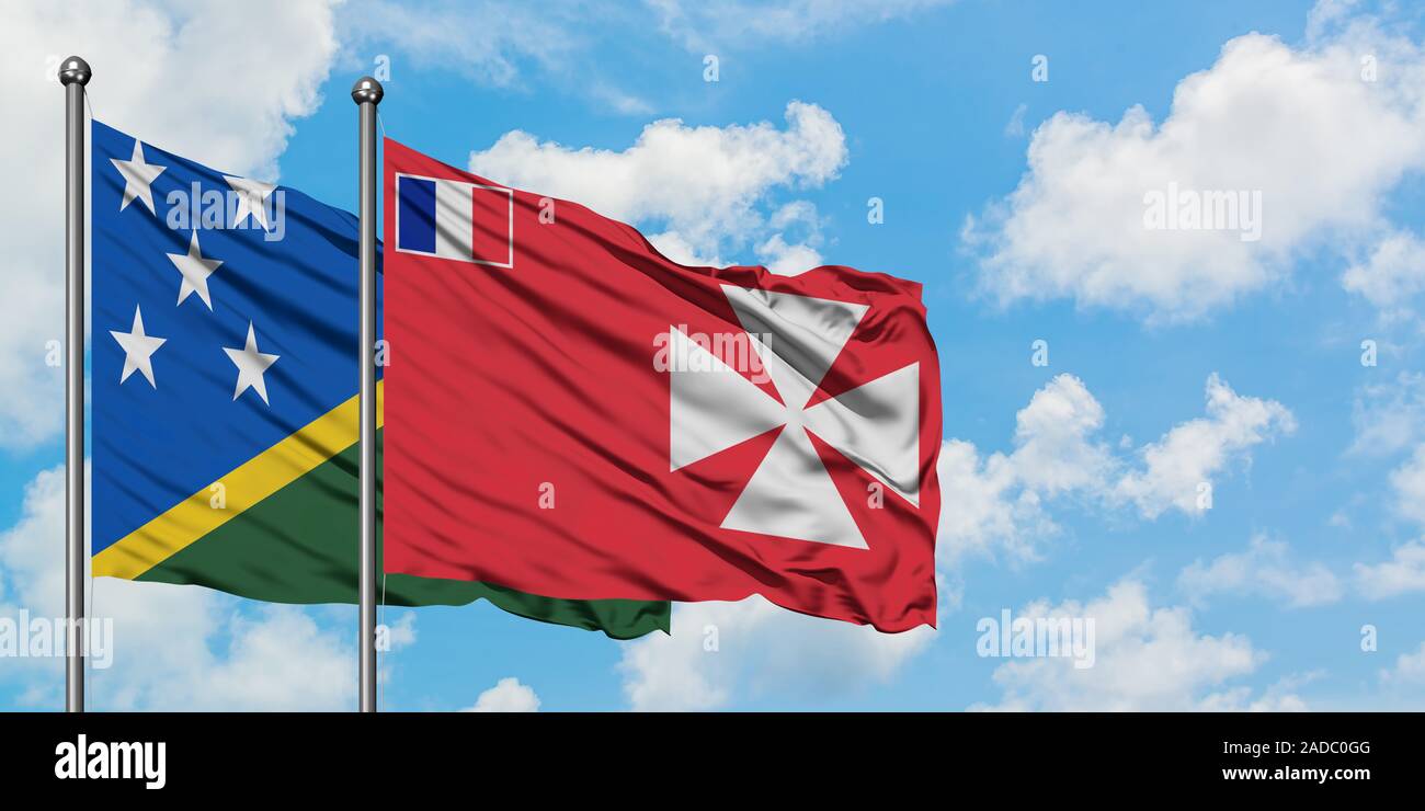 Solomon Islands and Wallis And Futuna flag waving in the wind against white cloudy blue sky together. Diplomacy concept, international relations. Stock Photo
