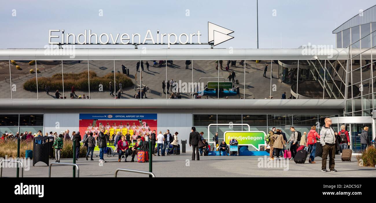Eindhoven Netherlands. October 14, 2019. People carrying luggage in front of Eindhoven airport terminal facade, sunny autumn day Stock Photo