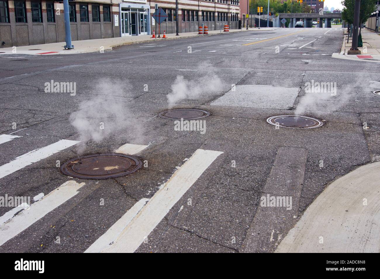 Steam escaping from underground pipes through vented manhole covers on