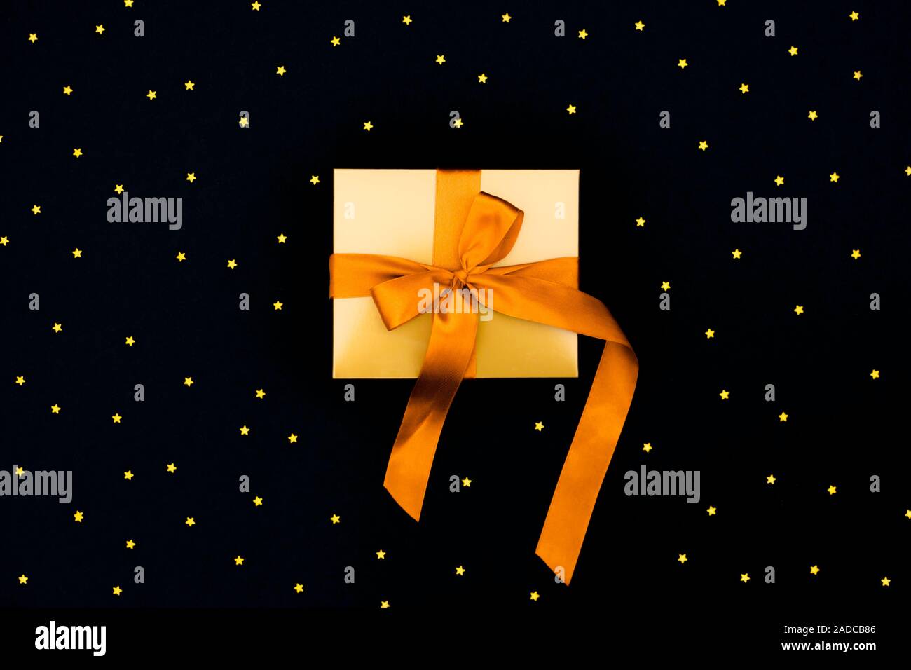 Gift gold box with a orange satin bow on the black background with lots