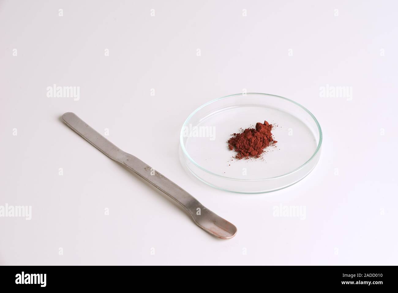 Iron III oxide powder in a glass petri dish and spatula isolated on white background. Science