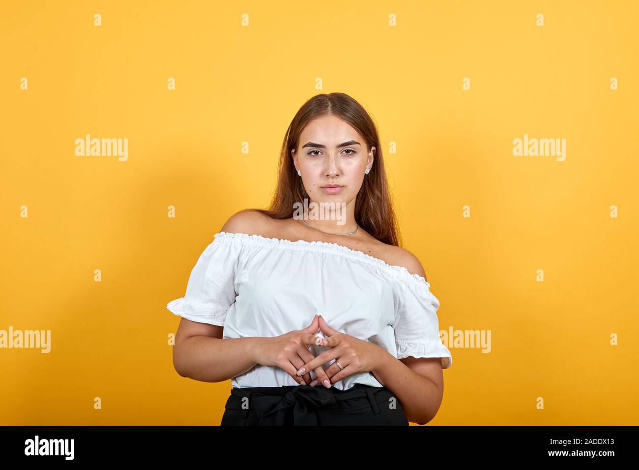 Strict young woman keeping hands together, looking at camera, serious ...