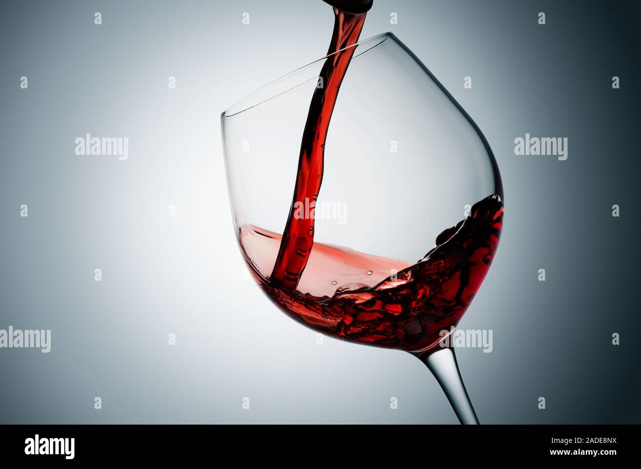 Pouring red wine into tilted glass, plain background. Stock Photo
